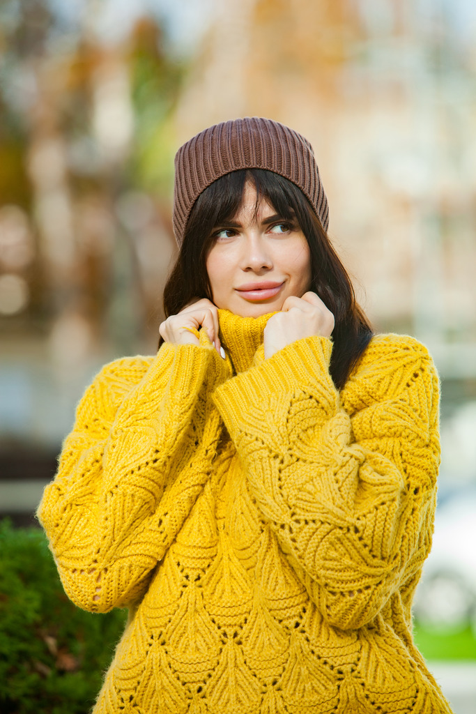 Beautiful European girl dressed in a yellow woolen cardigan and hat outside