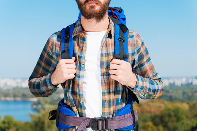 Close-up of young man carrying backpack while standing against urban scenery